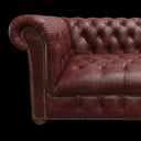 A close-up of a dark reddish-brown leather Chesterfield sofa with button tufting and brass nailhead trim, shown against a transparent checkerboard background.