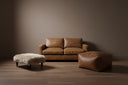 Brown leather sofa and ottoman with a textured wall in a dimly lit room.